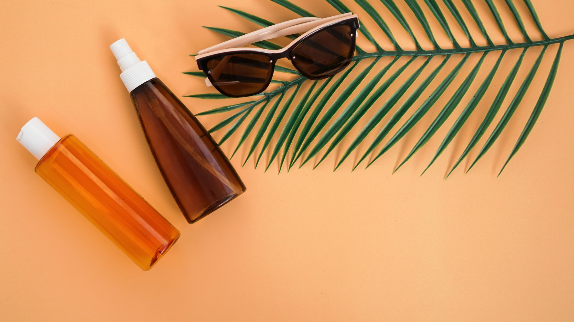 sunglasses-sun-lotion-palm-leaves-flat-lay-top-view-soft-orange-background